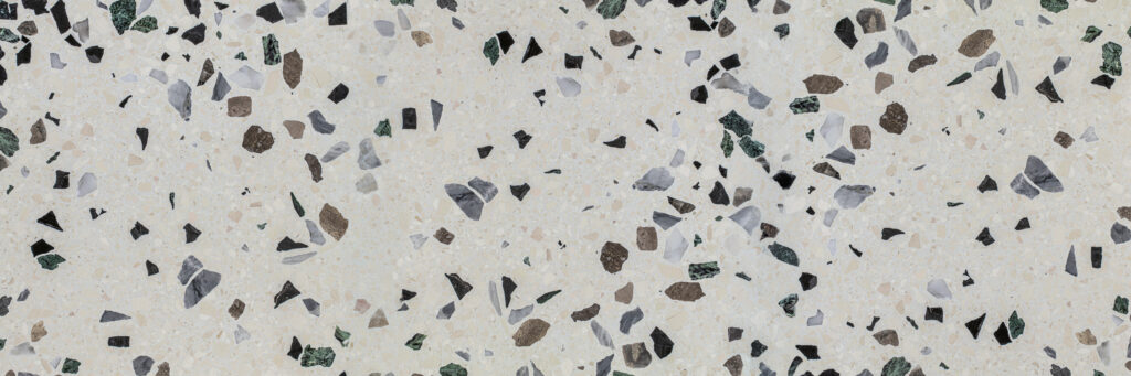 Terrazzo floor pattern with scattered chips in green, black, gray, and brown on a beige base.