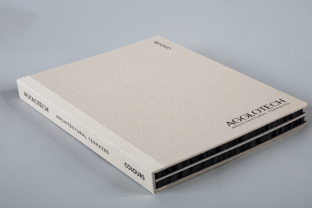 Beige hardcover sample book with 'COLOURS' and 'ARCHITECTURAL TERRAZZO' text, shown at an angle on a gray surface.
