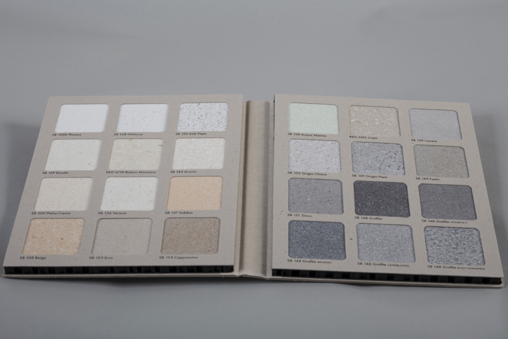 Open paint swatch book showing two pages of square color samples in light neutrals, each labeled with color codes like SB 1000 Thassos and SB 158 Acqua Marina.