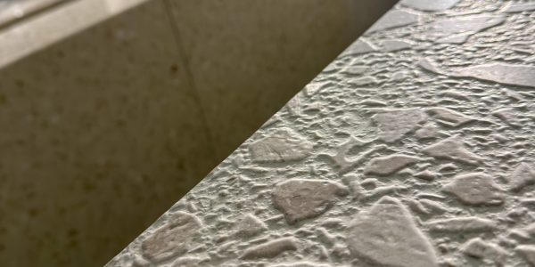 Close-up of a textured stone wall with a diagonal seam creating two lighter and darker areas.