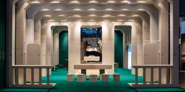 Symmetrical exhibition scene with layered beige archways, teal carpet, and a central display featuring a glossy AGGLOTECH poster.
