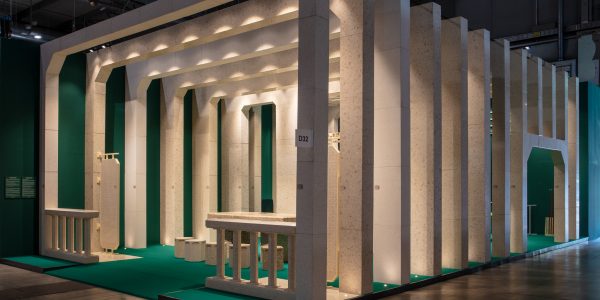 Exhibition hall with a row of limestone-like arches and columns on a green floor, creating a tunnel effect.