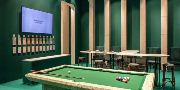 Pool table in a green-walled lounge with terrazzo edges and color swatches mounted on the wall beneath a blue display screen.