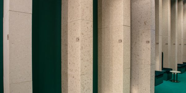Row of tall beige terrazzo columns in a teal gallery space.