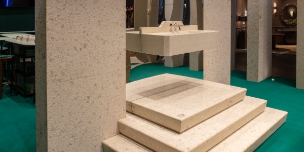 Beige terrazzo staircase with a built-in sink and dual taps, surrounded by stone columns in a modern showroom showfloor terms of use.